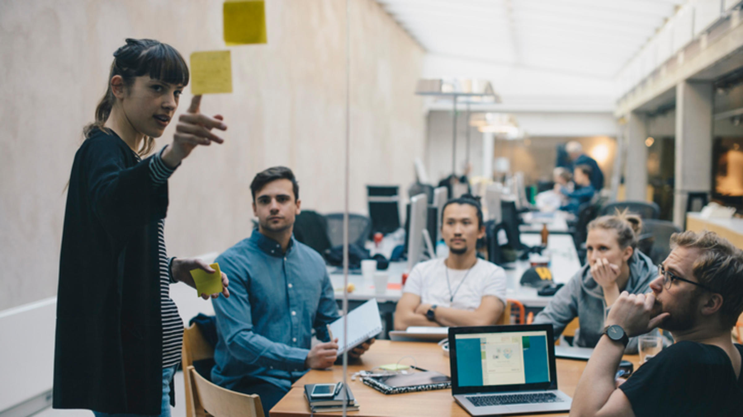 group of twenty and thirty year old coworkers looking at a woman pointing to a post-it note