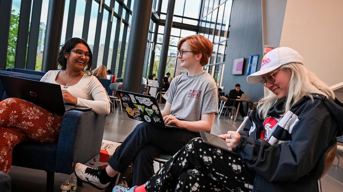 Image of students talking while having their laptops on their laps.