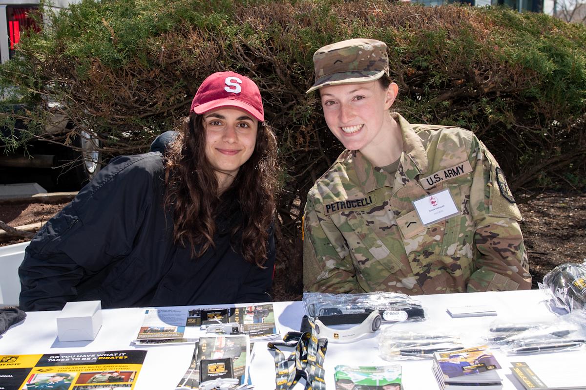 Students at table, one in uniform, share information about military programs at Stevens