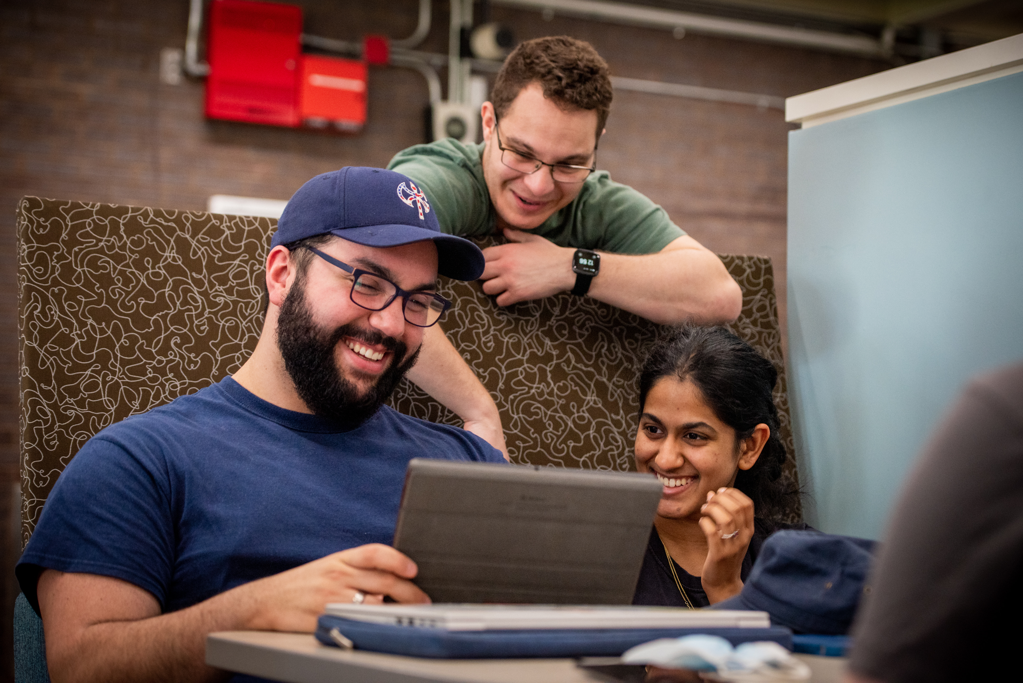 3 students smiling and working on tablet