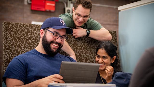 3 students smiling and working on tablet