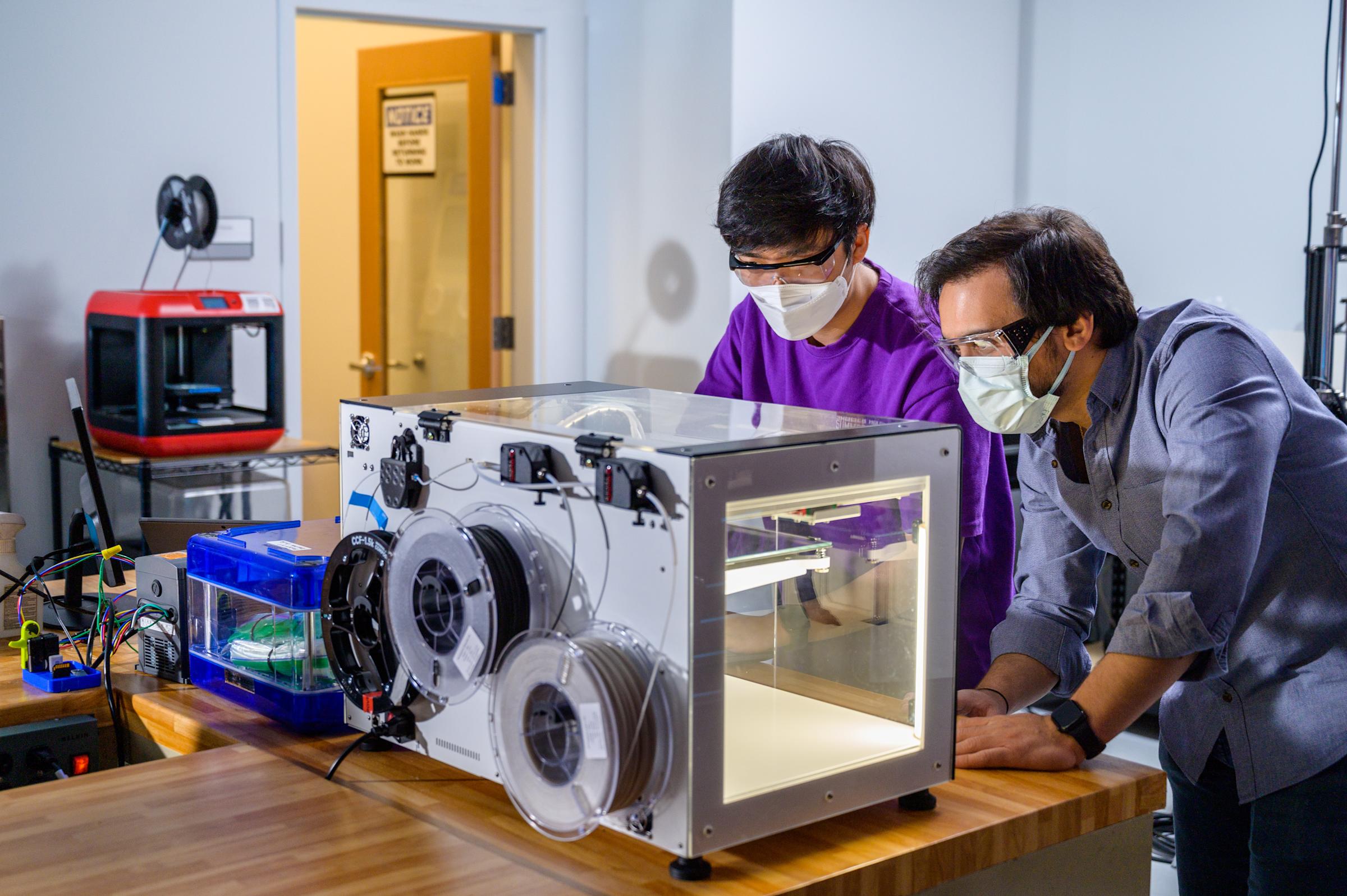 Two students using a 3D printer in the proof lab.