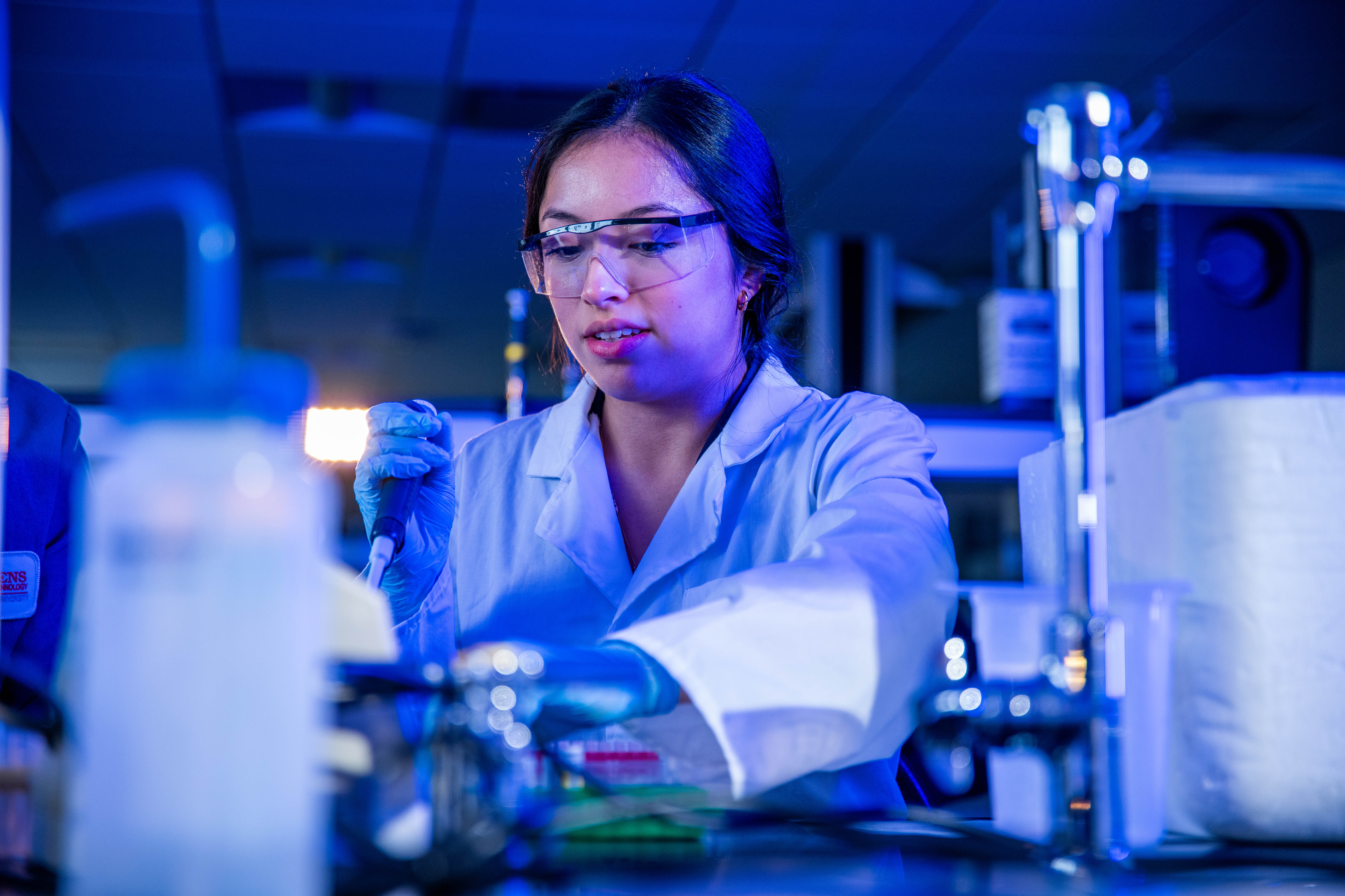 A female student working in a blue-lit chemistry laboratory.