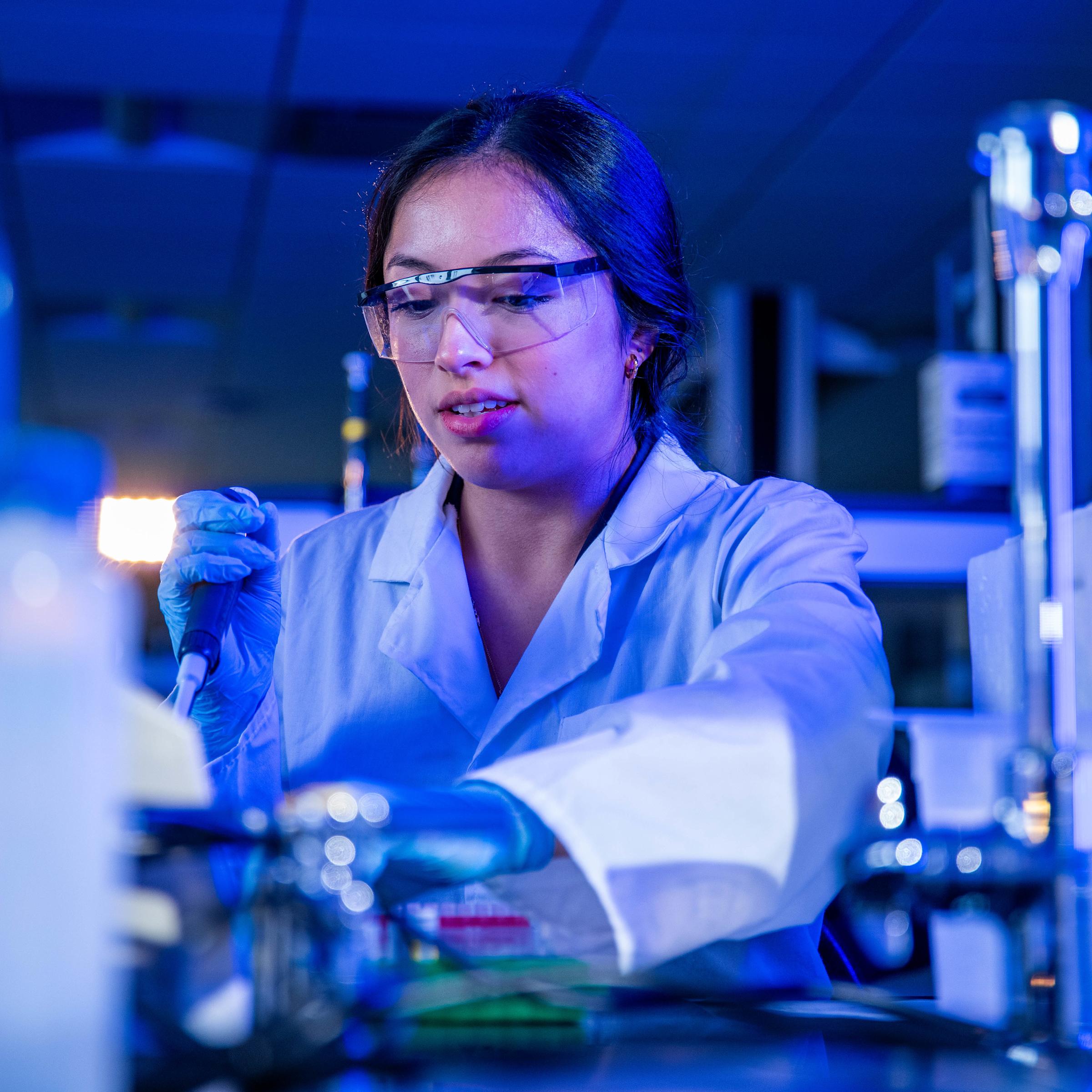 A female student working in a blue-lit chemistry laboratory.
