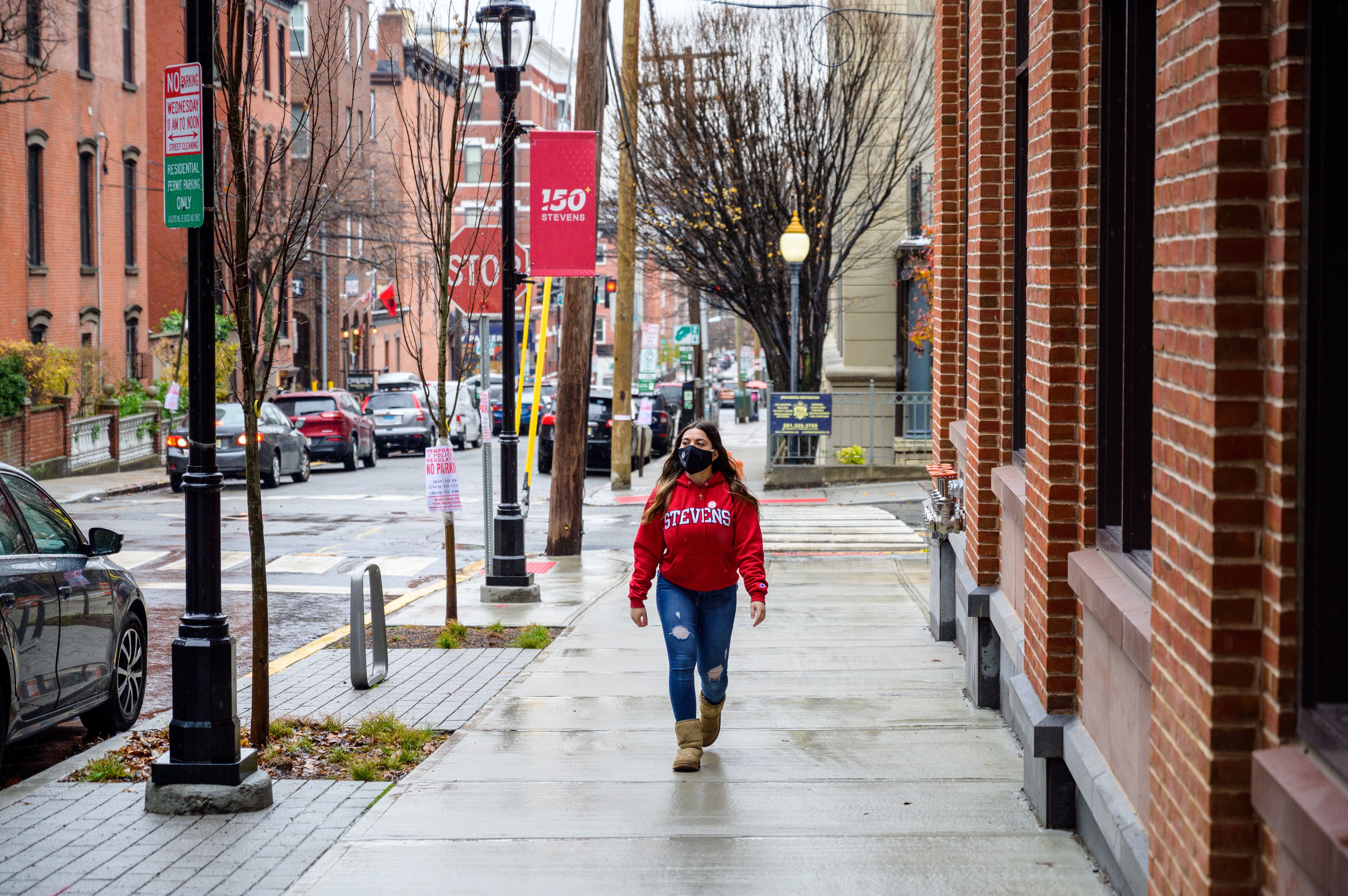 Female Stevens student in red hoodie walking on a Hoboken sidewalk after a rainshower.