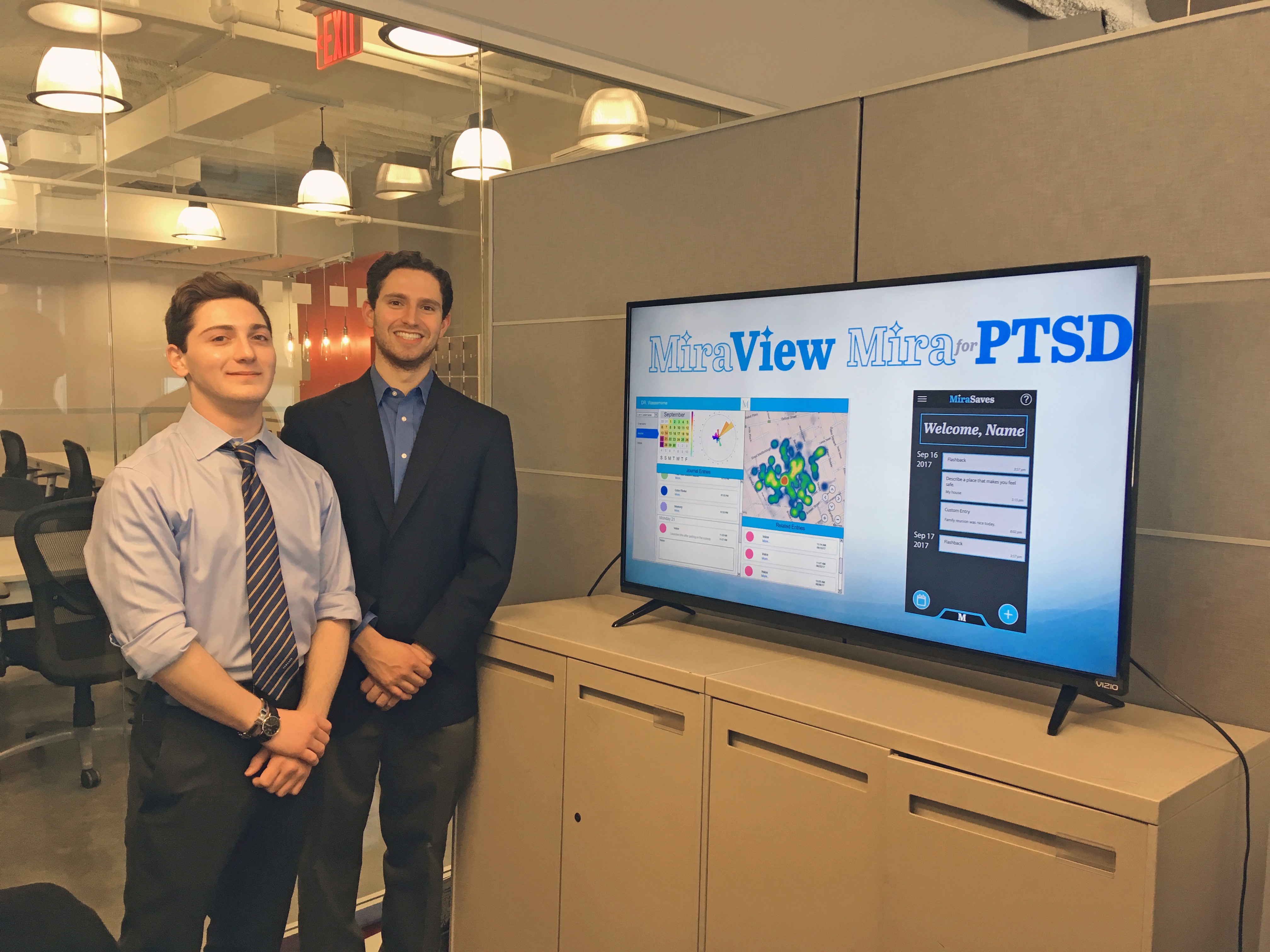 The two students behind MiraView in the Stevens Venture Center alongside a monitor showing their app's capabilities.