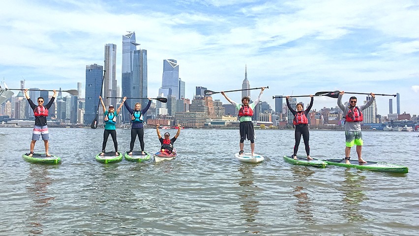 Stevens students on paddleboards on the Hudson River, with the Manhattan skyline in the background.