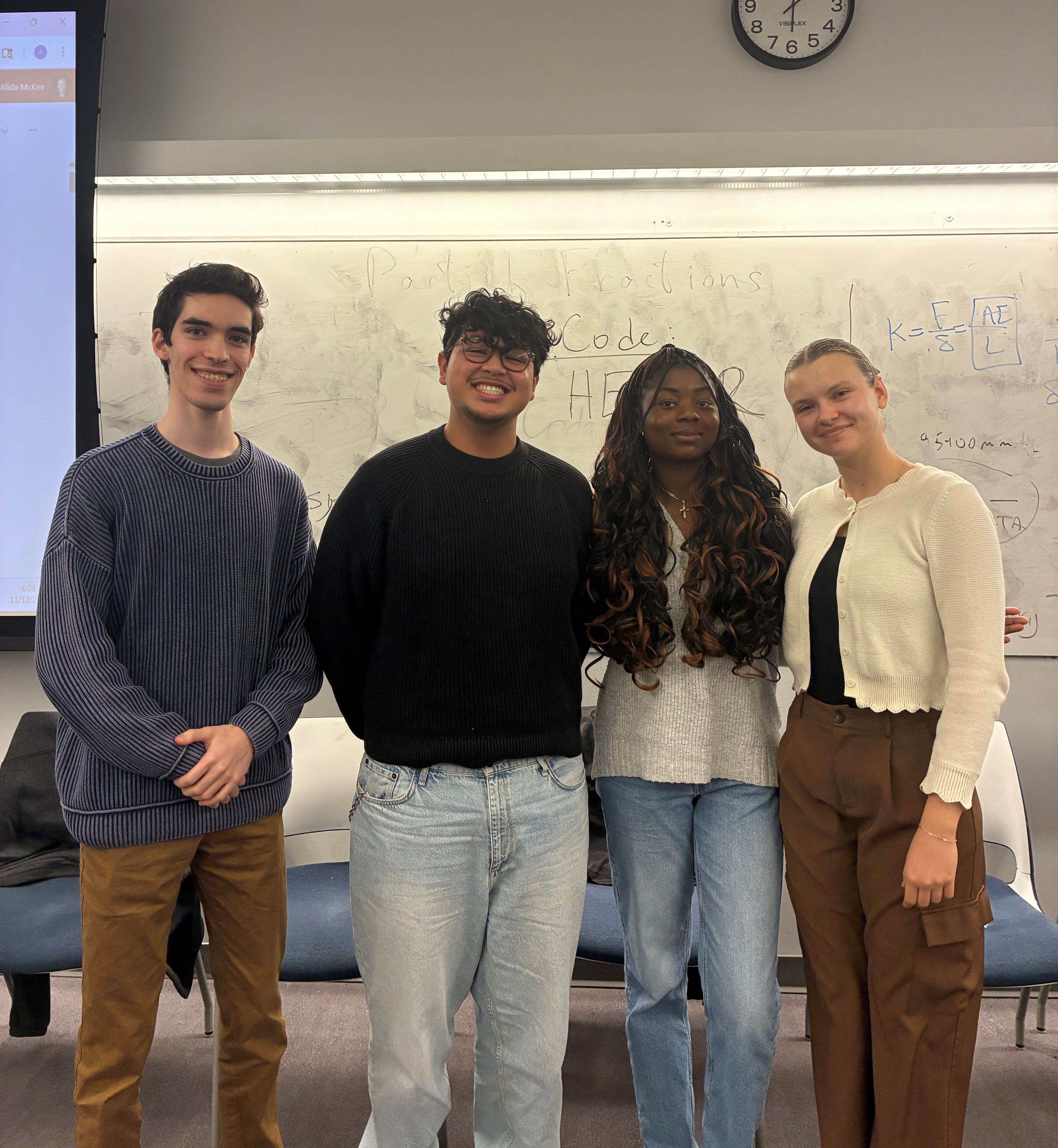 Four Pinnacle Scholars students stand together in a classroom, posing in front of a whiteboard. 
