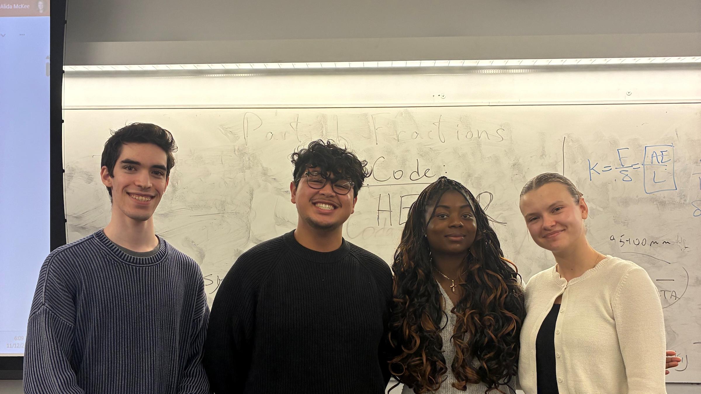 Four Pinnacle Scholars students stand together in a classroom, posing in front of a whiteboard.