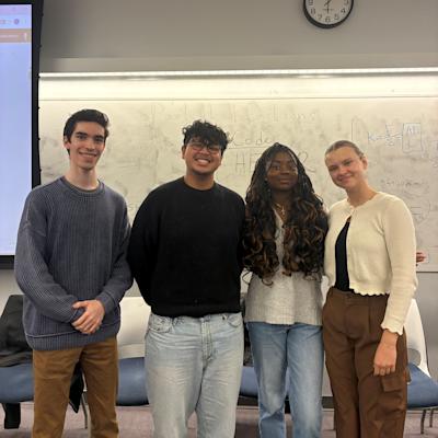 Four Pinnacle Scholars students stand together in a classroom, posing in front of a whiteboard.