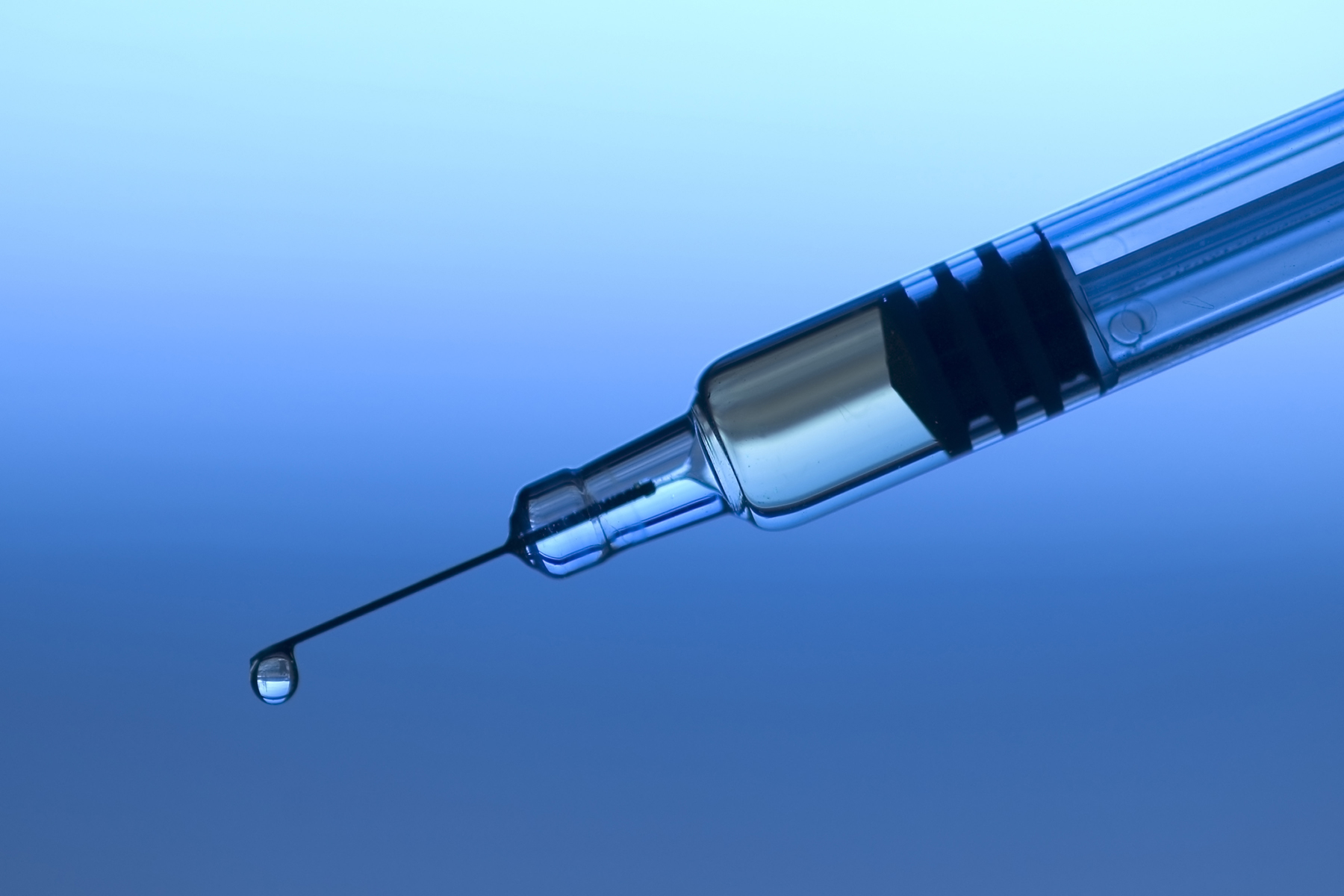 A photo of a syringe with a droplet coming out of the tip of the needle. The background is blue.