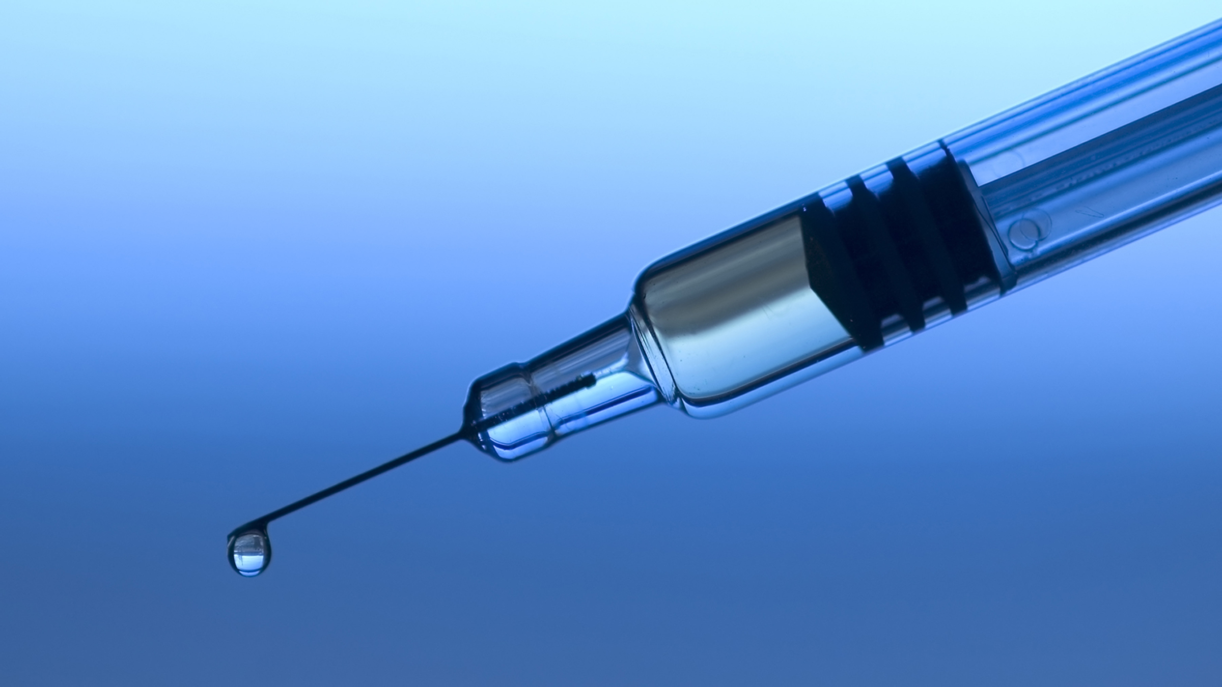 A photo of a syringe with a droplet coming out of the tip of the needle. The background is blue.