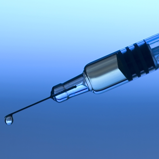 A photo of a syringe with a droplet coming out of the tip of the needle. The background is blue.