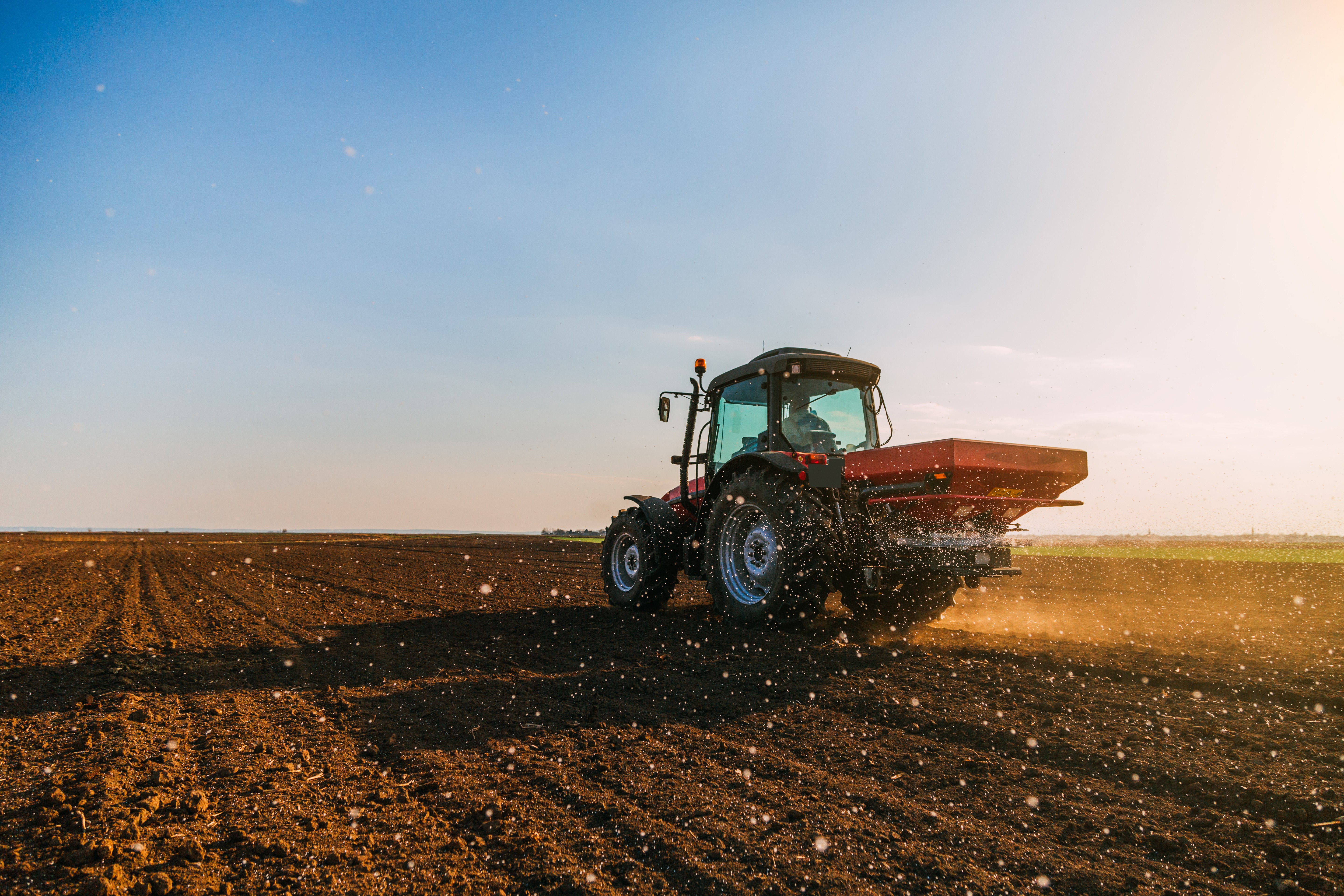 A red tractor fertilizing cropland under a blue sky