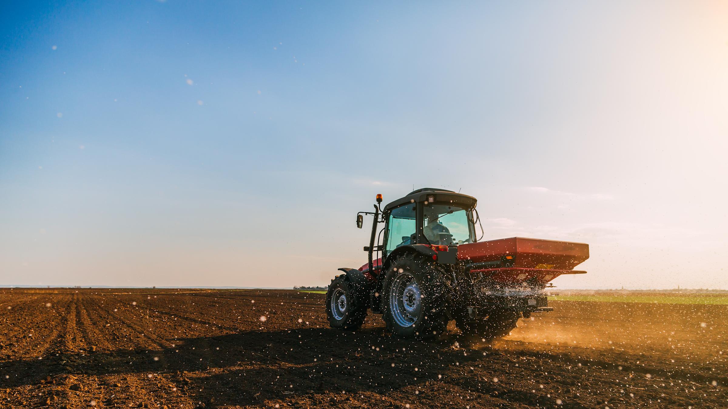 A red tractor fertilizing cropland under a blue sky