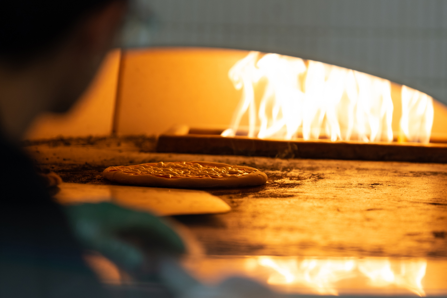 Chef places pizza in flaming hot oven.