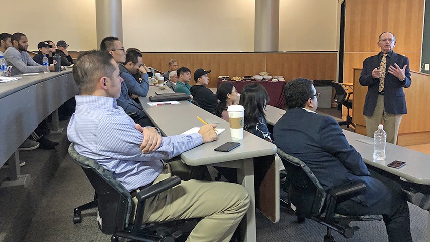 Gary Lilien speaks in a crowded auditorium as two rows of students listen and take notes.