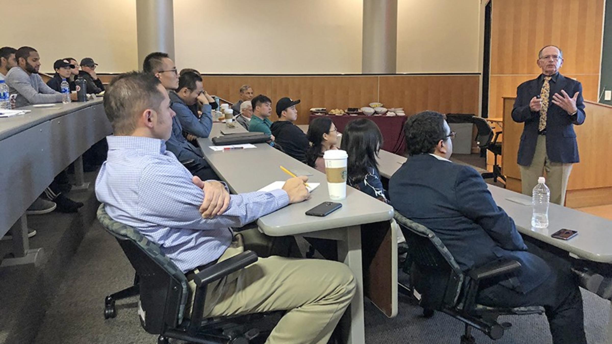 Gary Lilien speaks in a crowded auditorium as two rows of students listen and take notes.
