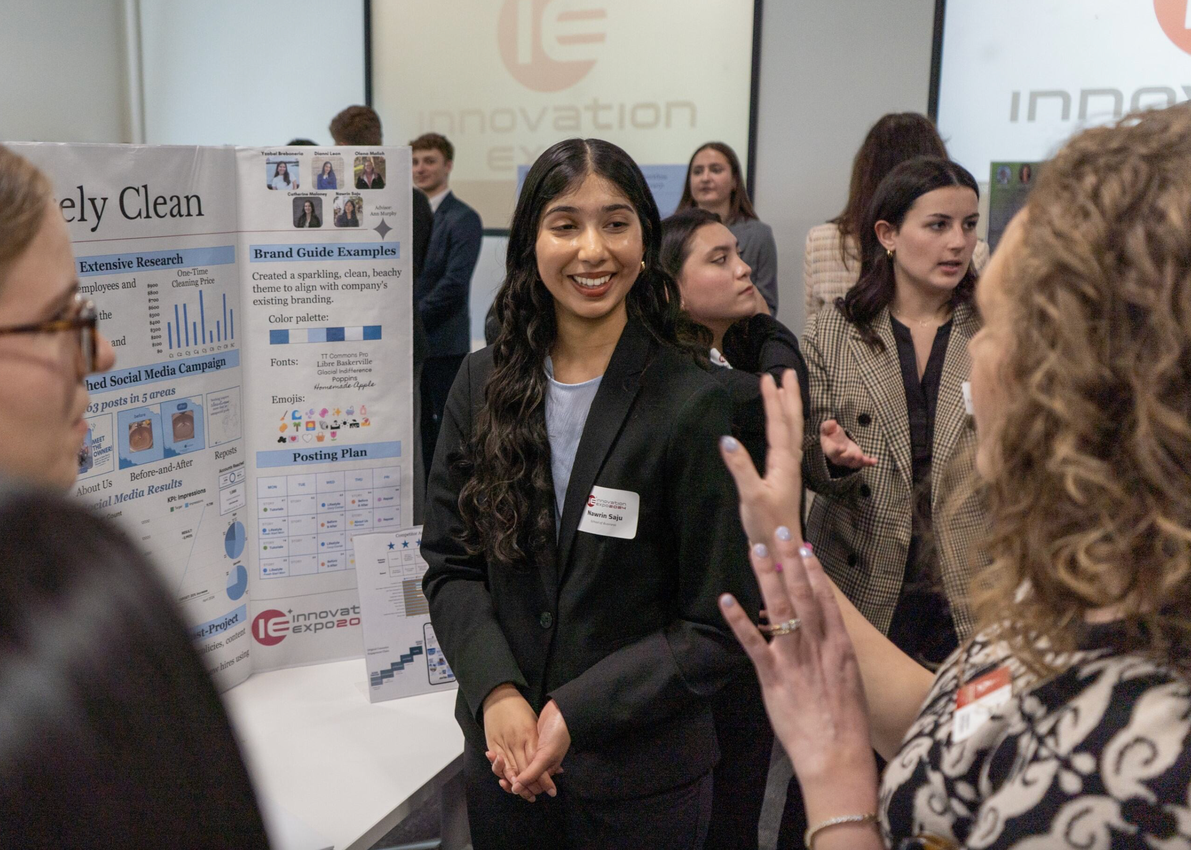 A member of the Shorely Clean team, wearing a black pantsuit speaks to someone while standing in front of their posterboard.