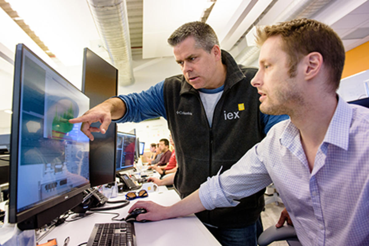 Two men in professional attire point to a Bloomberg terminal