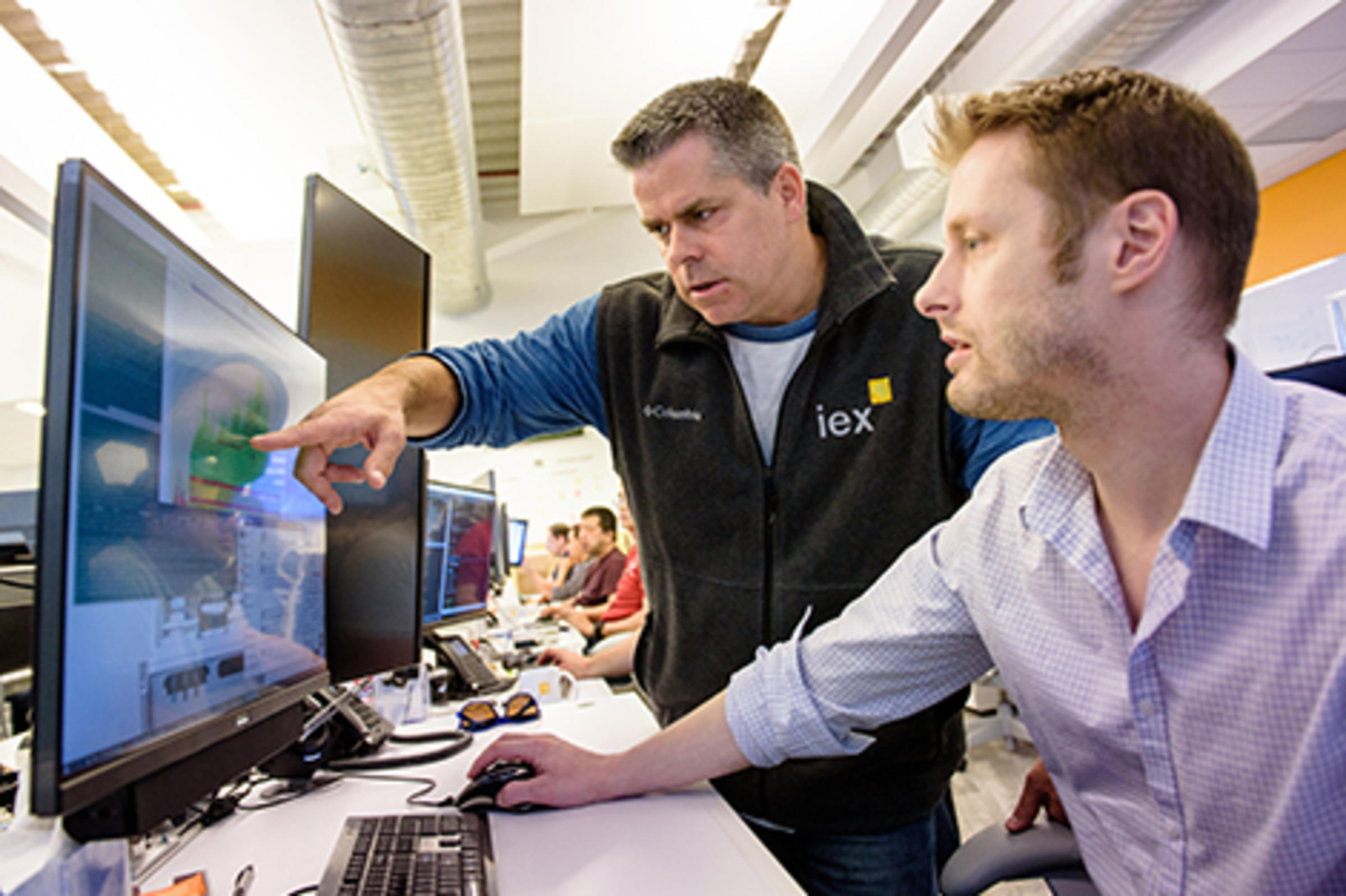 Two men in professional attire point to a Bloomberg terminal