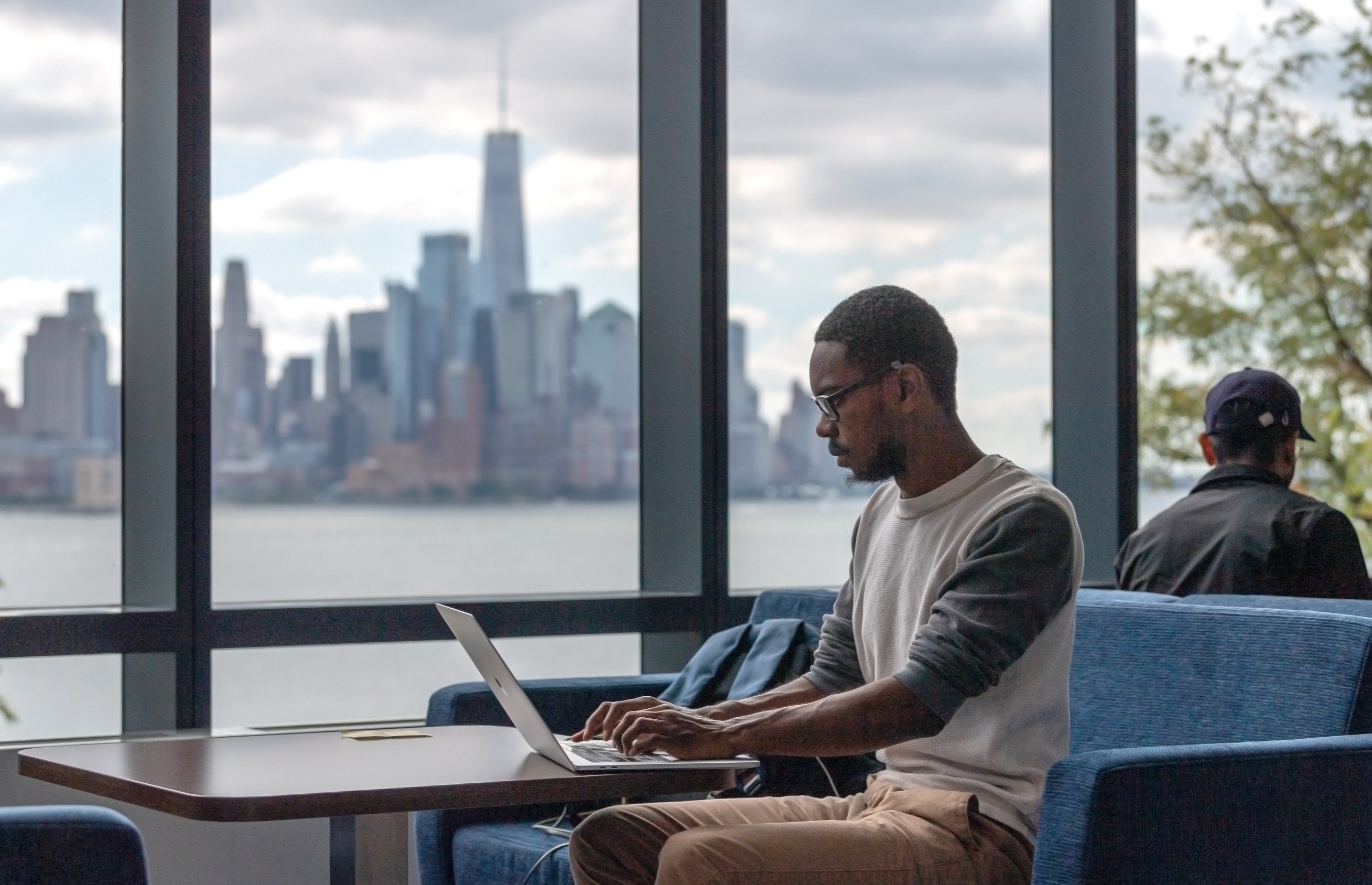 Student works on laptop in the UCC with New York city skyline in background.