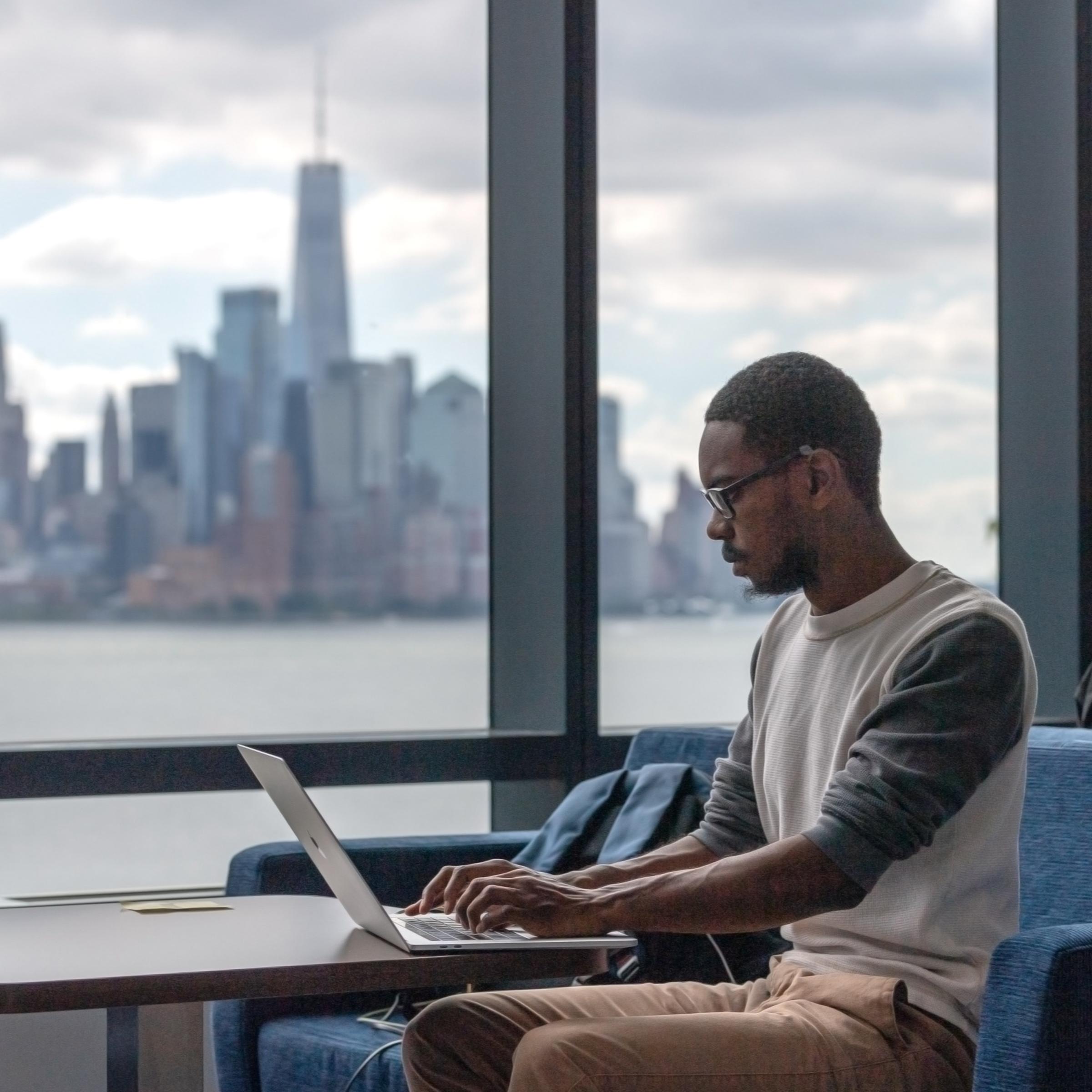 Student works on laptop in the UCC with New York city skyline in background.