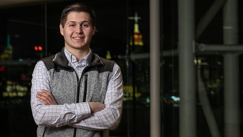 A male student poses in front of the bright lights of New York City at night.