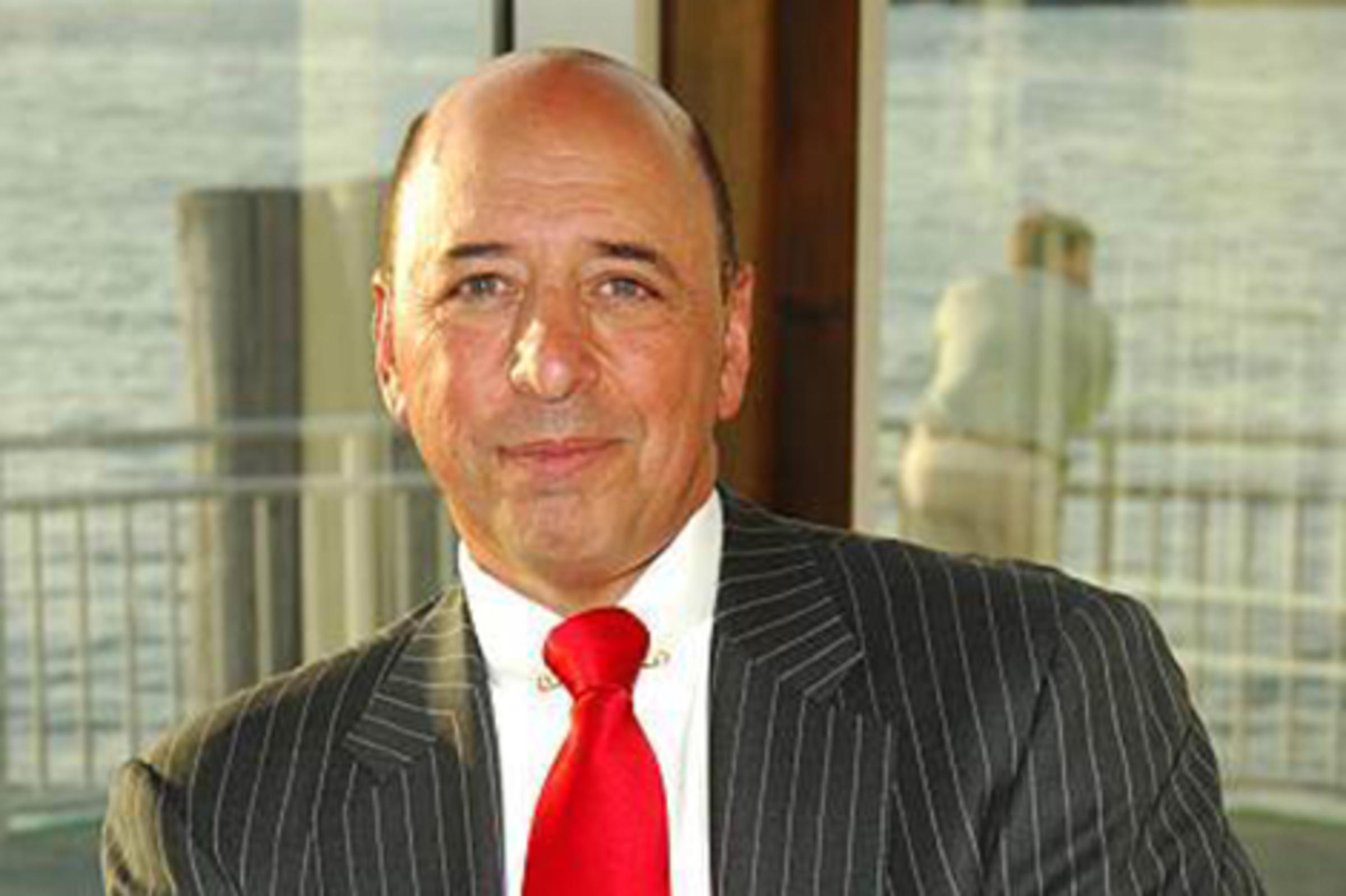 Fran Dramis seated, wearing a pinstriped suit with a red tie.