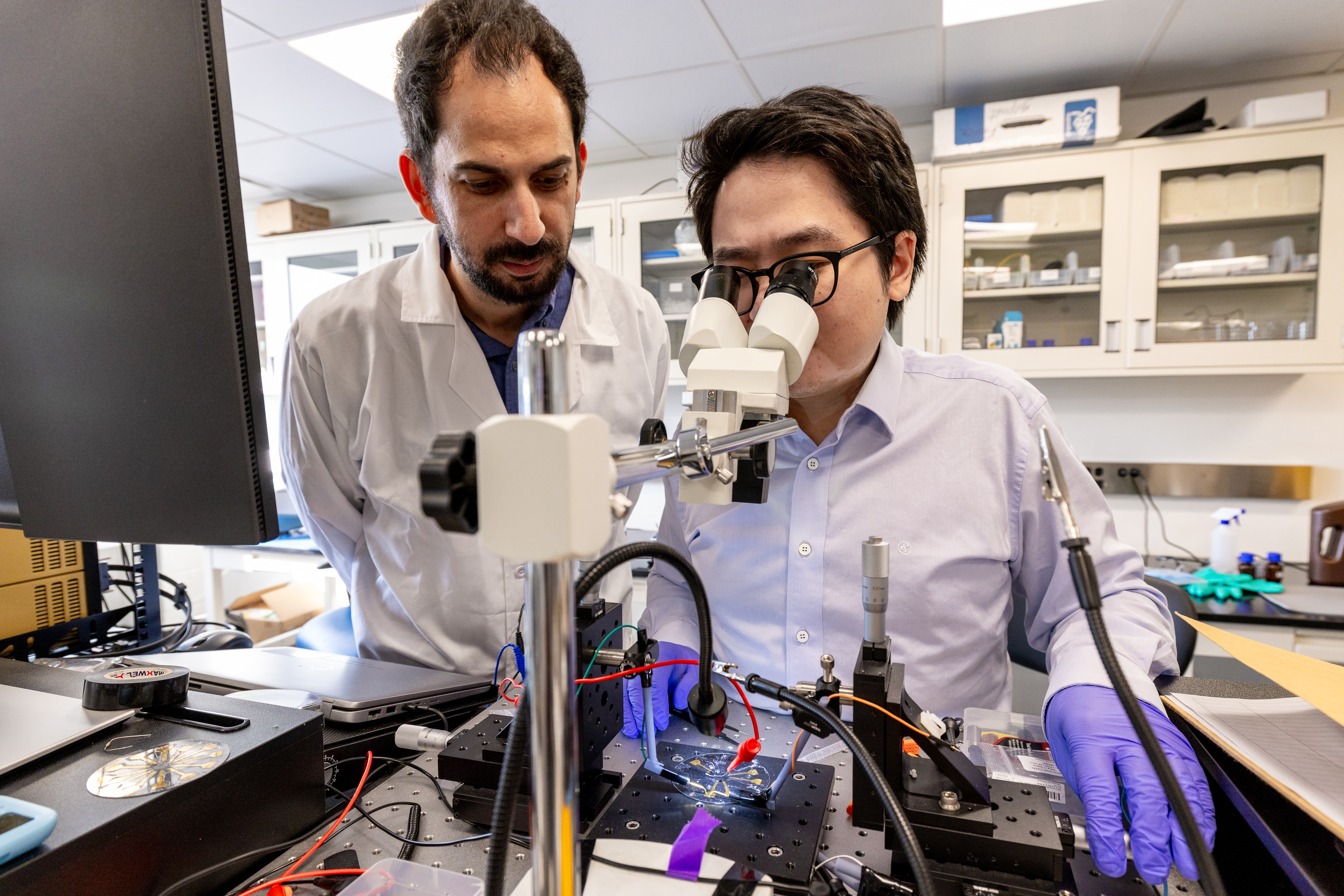 A researcher and a student looking through a device in a lab.