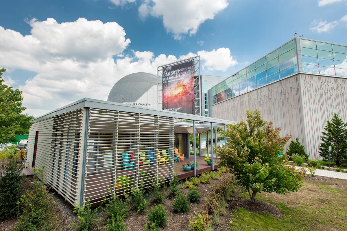Photo of the SU+RE House at Liberty Science Center on a sunny day with green trees around it 