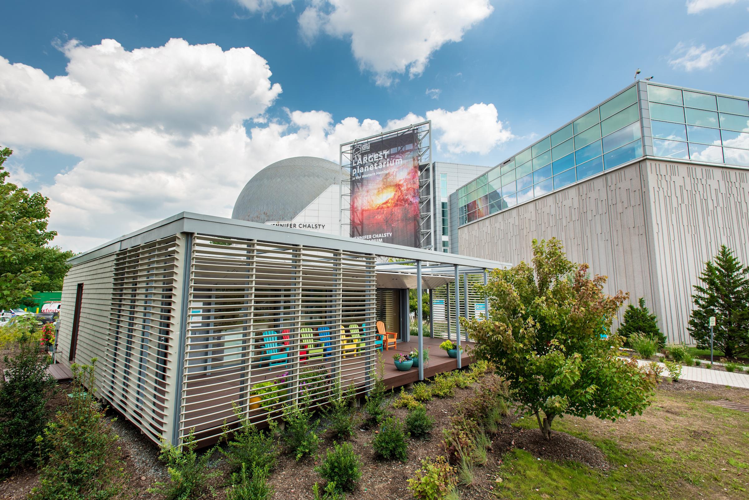 Photo of the SU+RE House at Liberty Science Center on a sunny day with green trees around it