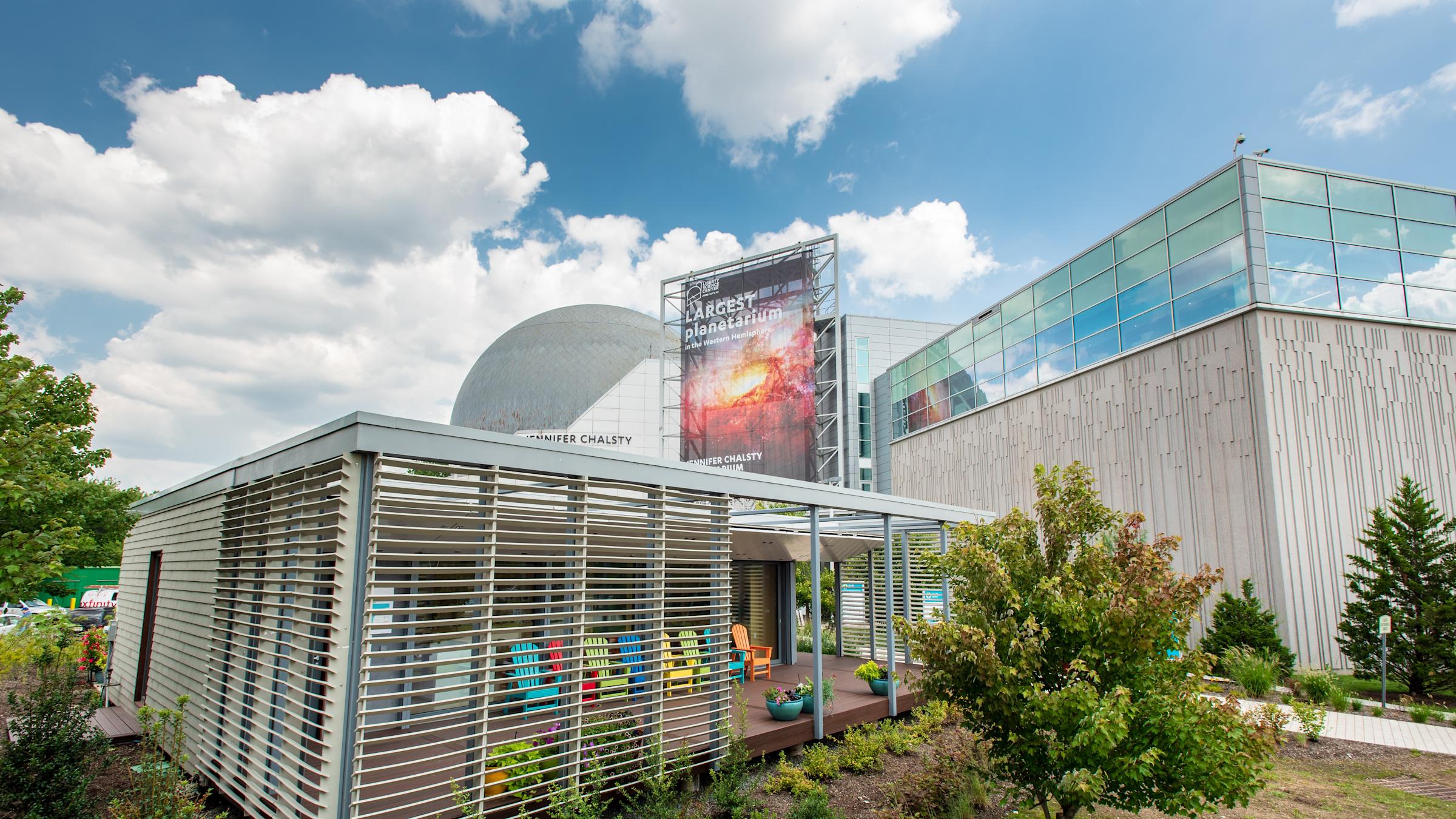 Photo of the SU+RE House at Liberty Science Center on a sunny day with green trees around it