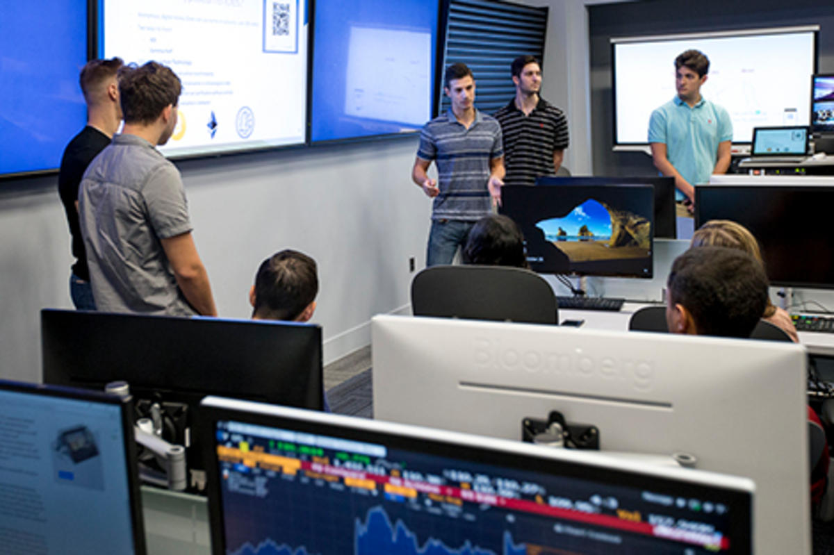 A group of freshmen present a project on cryptocurrency in the Hanlon Lab at Stevens. Bloomberg terminals are visible in the foreground.