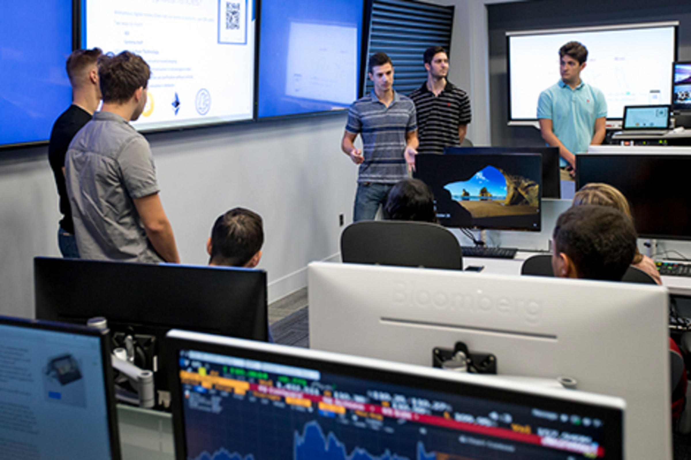 A group of freshmen present a project on cryptocurrency in the Hanlon Lab at Stevens. Bloomberg terminals are visible in the foreground.