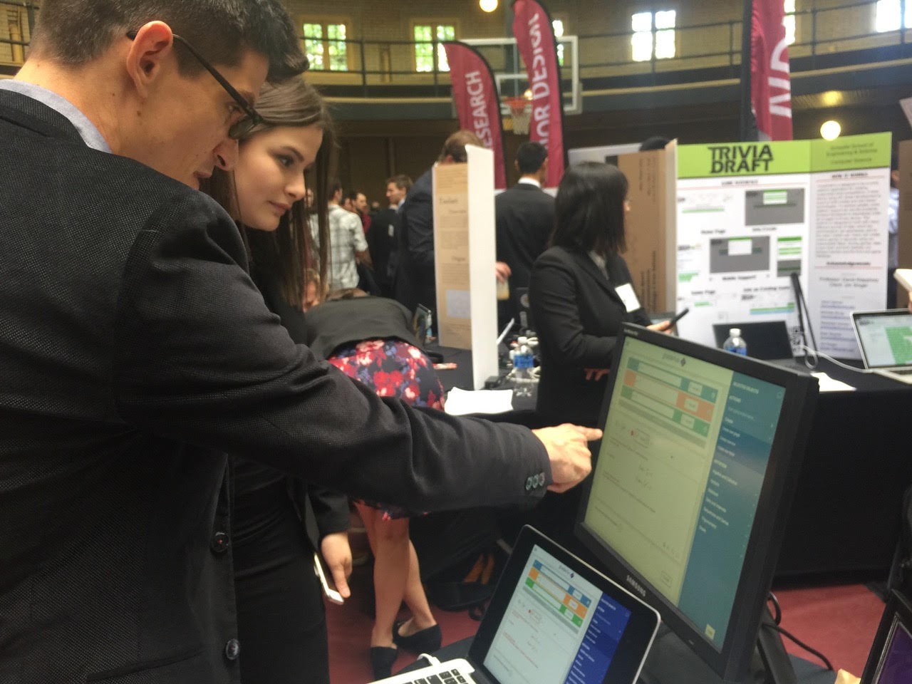A male professor points at a computer screen while a female student watches
