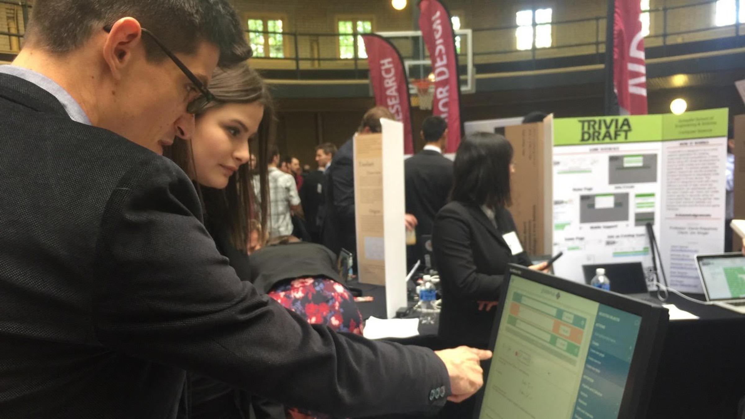 A male professor points at a computer screen while a female student watches