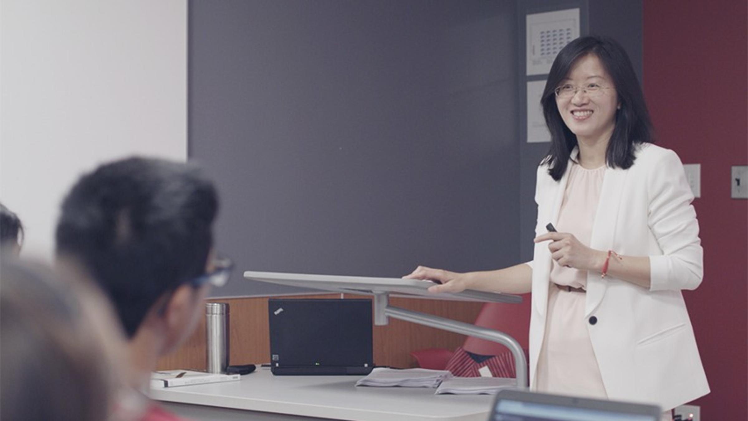 Prof. Ying Wu teaches her international finance class. She's standing in front of the room, answering a student's question.