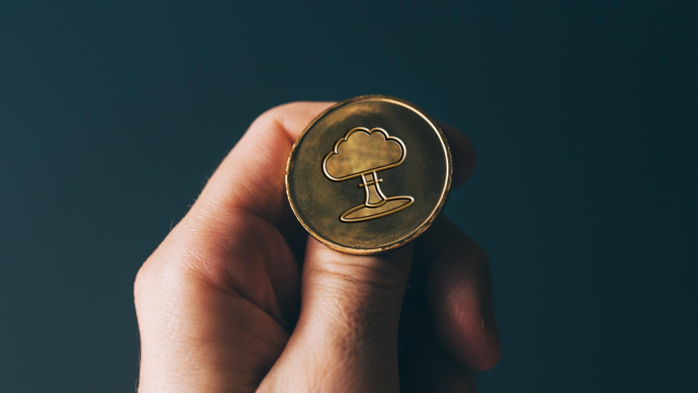 An image featuring a hand about to flip a coin. The coin features a plume - what you would see after a nuclear weapons detonation