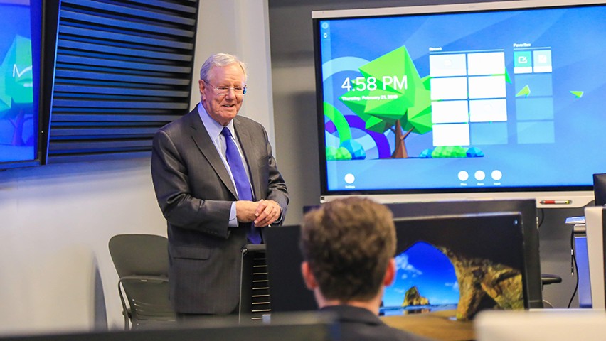 Steve Forbes talks to students in the Hanlon Lab. A number of screens and Bloomberg terminals can be seen.