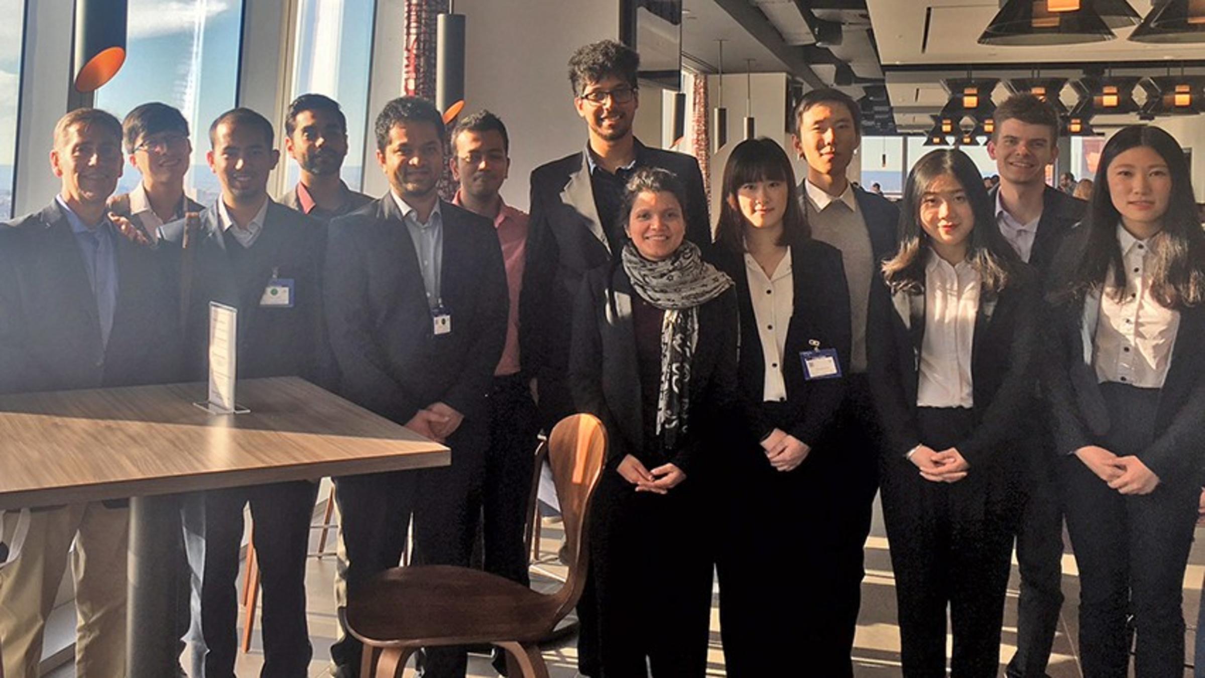 A group of men and woman in business attire posed for a photo with the New York City skyline visible in the background.