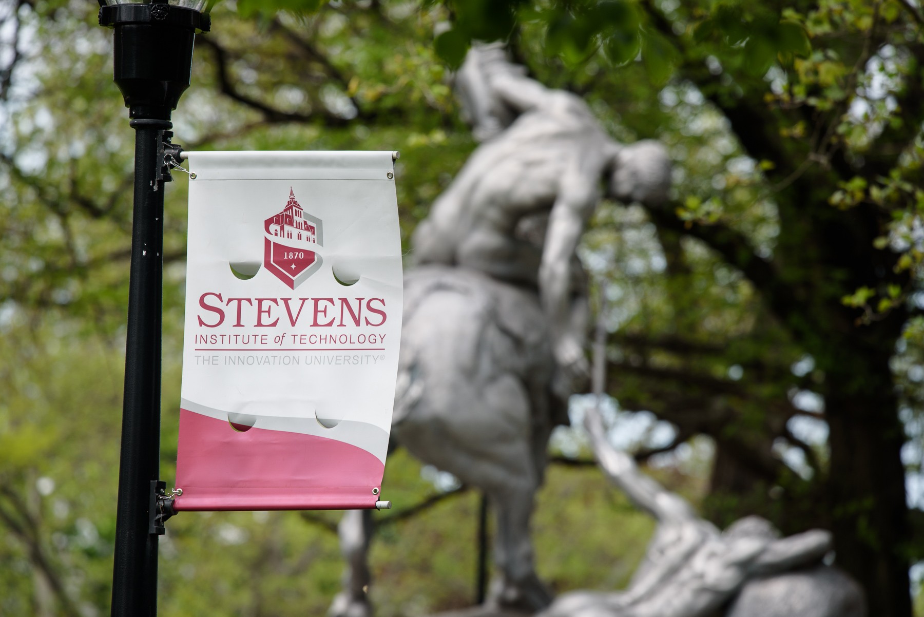 Stevens logo flag in front with torch bearer statue in background