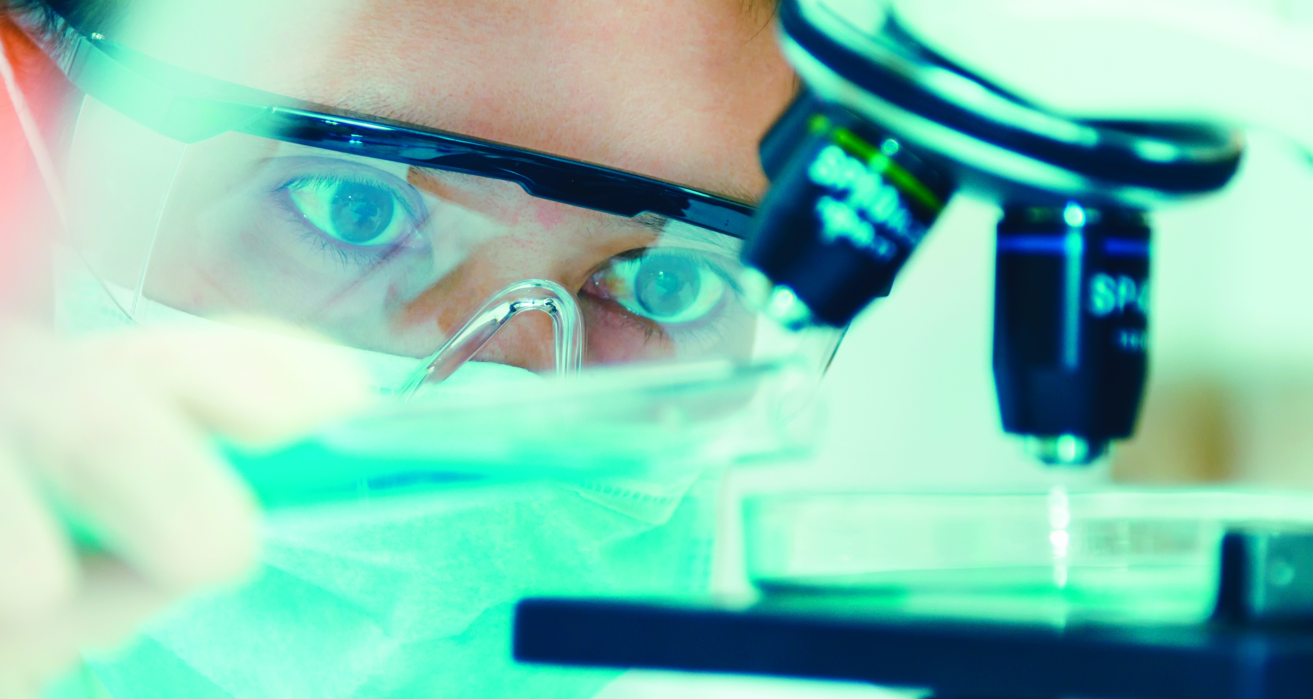 A woman in a clean suit views a sample under a microscope