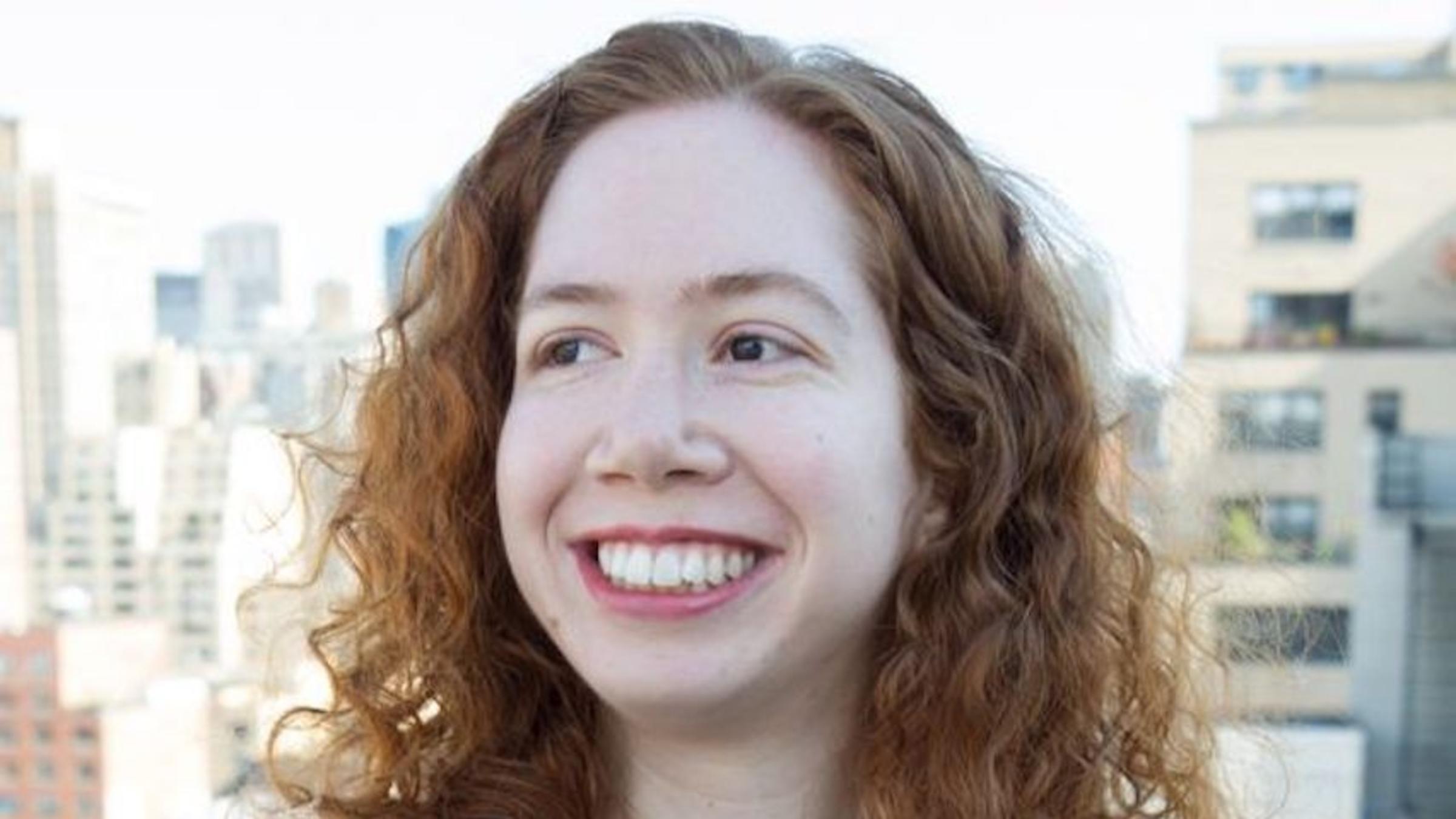 Picture of Samantha Kleinberg in black short-sleeved shirt. She is white with red hair and she is smiling.