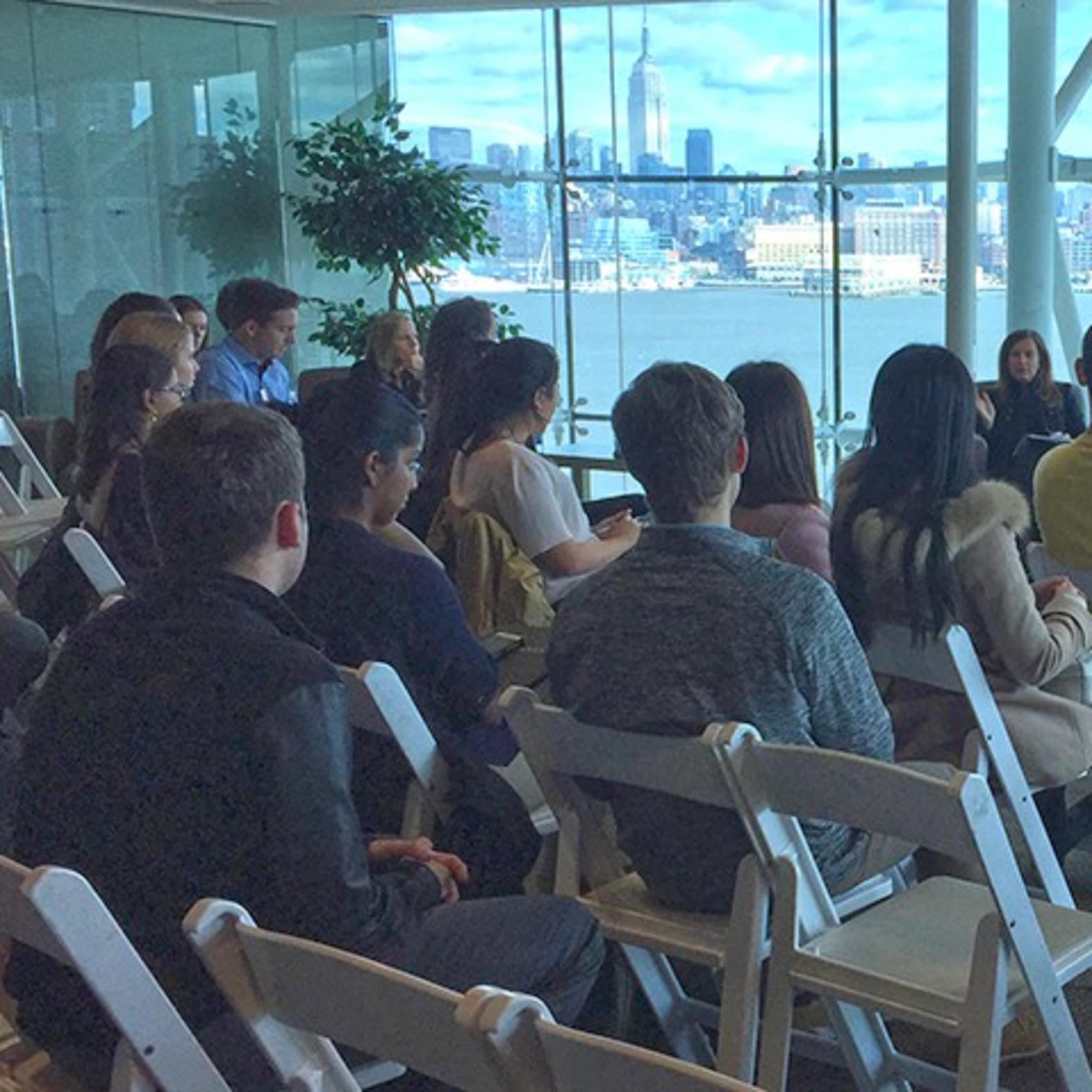 Panelists address a room packed with students in the Babbio Center at Stevens. The New York skyline is visible in the background.