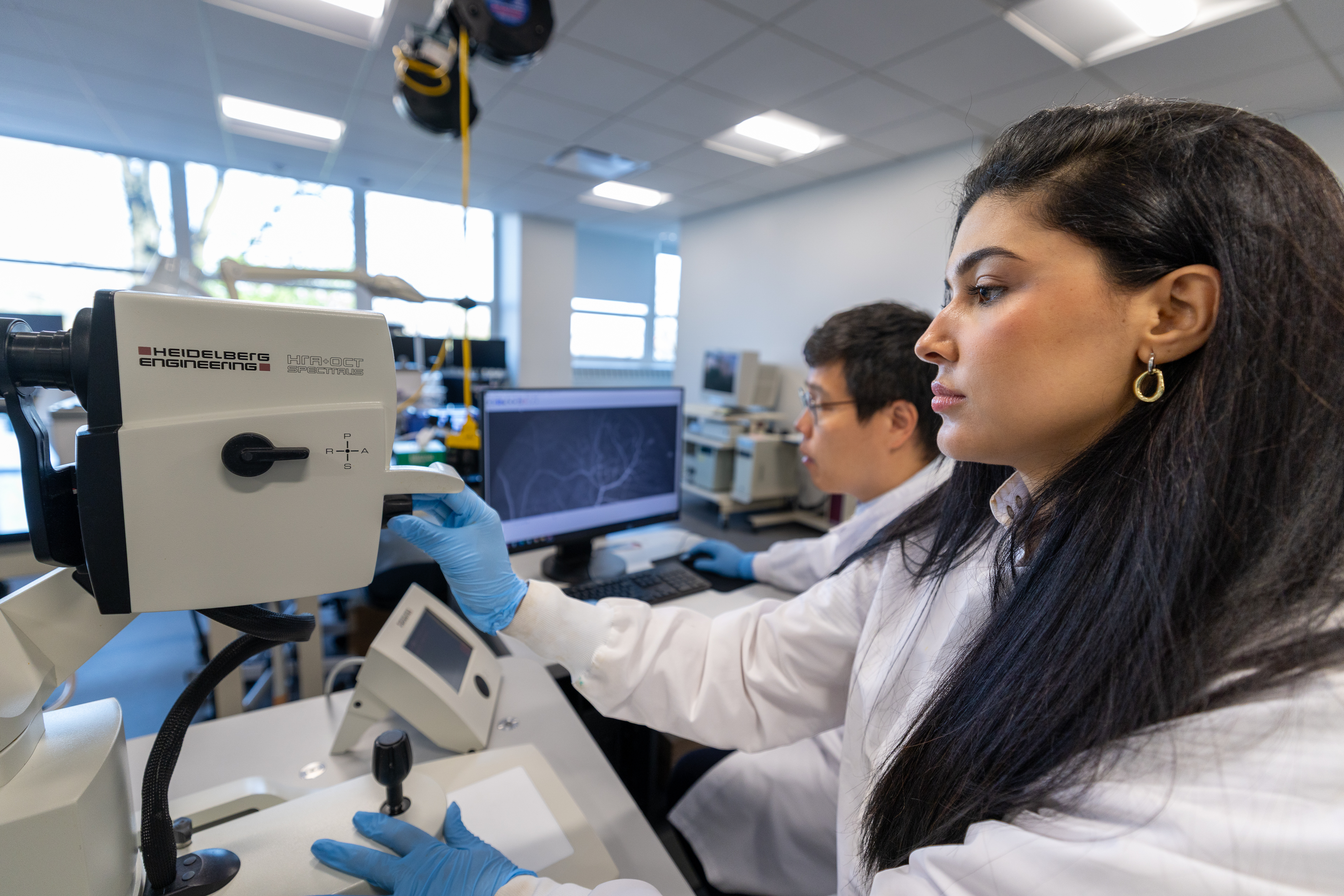 A woman and a man work with a microscope and computer.