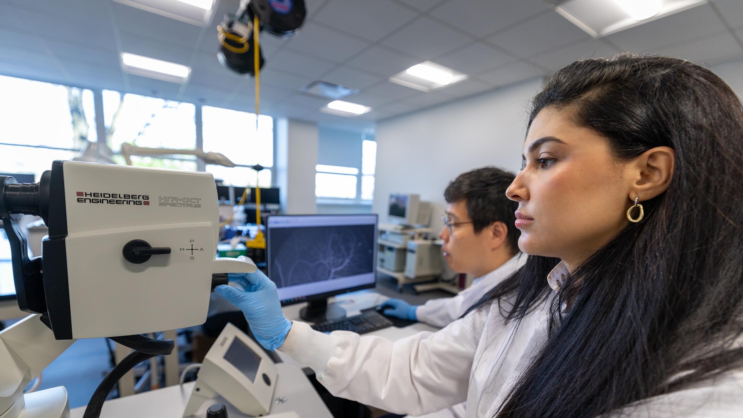 A woman and a man work with a microscope and computer.