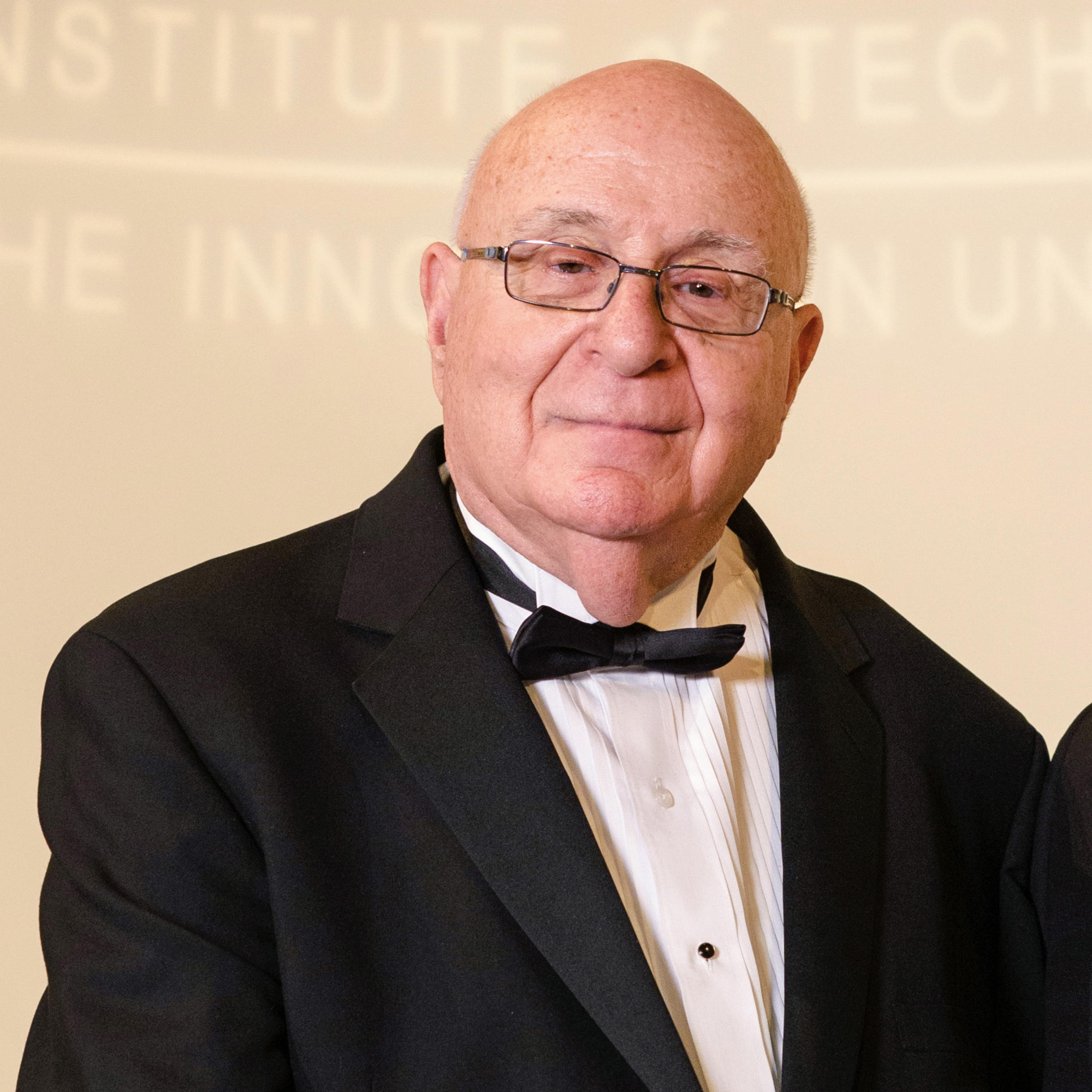Photo of Dave Farber ’56 M.S. ’61, left, being presented a plaque by Stevens President Nariman Farvardin on a stage, with the Stevens logo and name projected in the background.
