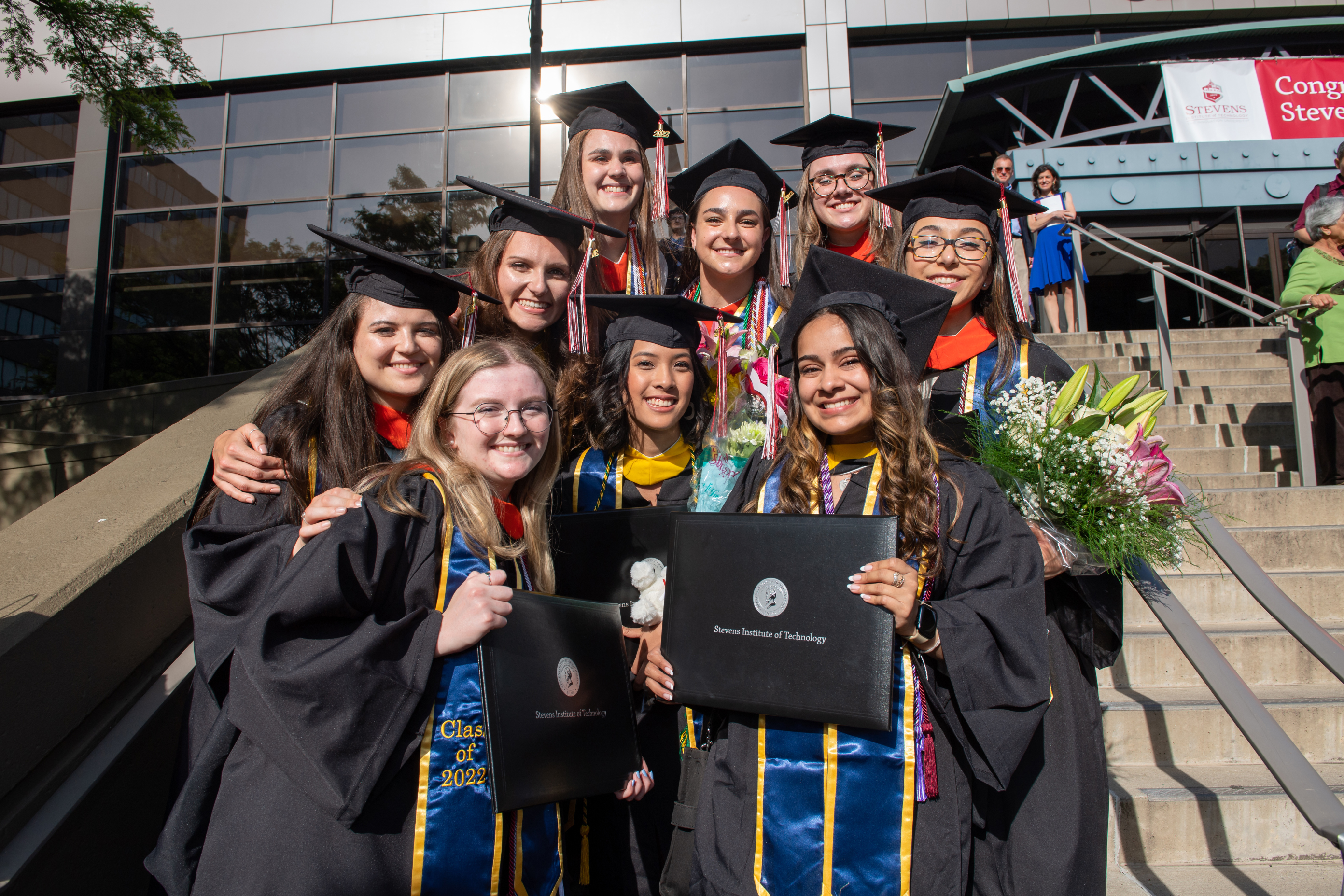 Group of students in caps and gowns smiling outside commencement hall.