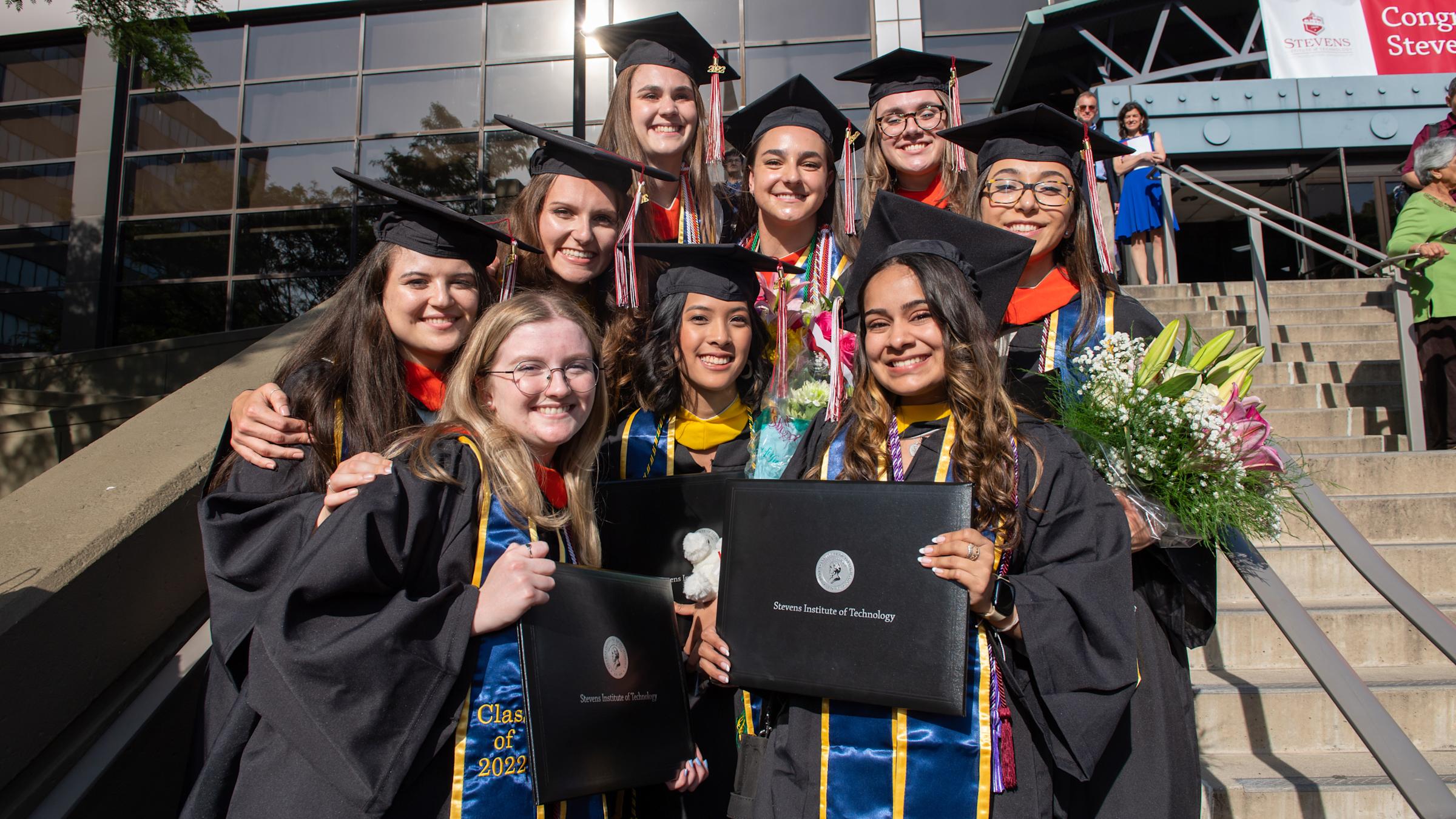 Group of students in caps and gowns smiling outside commencement hall.